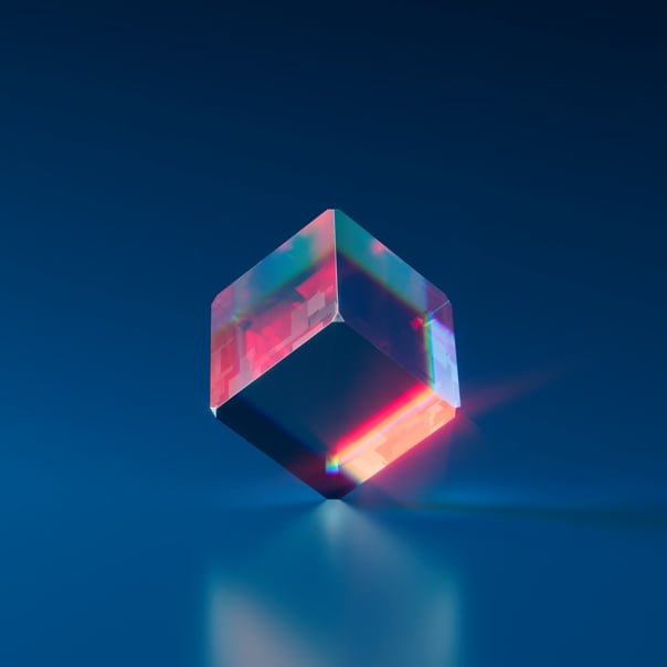 A clear cube
            reflecting red and blue light, balanced on one corner on a flat
            blue surface.